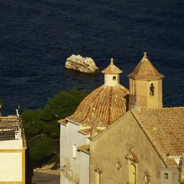 Terracotta-tiled dome and bell tower of a church in Ibiza's old town, with a ferry crossing dark blue sea beyond.
