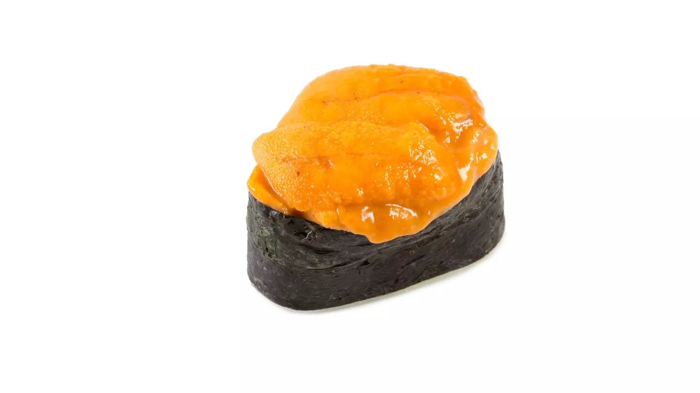 A hand holding Uni Gunkan at Sake no Hana. Orange sea urchin sits on a bed of rice wrapped in seaweed topped with fresh wasabi