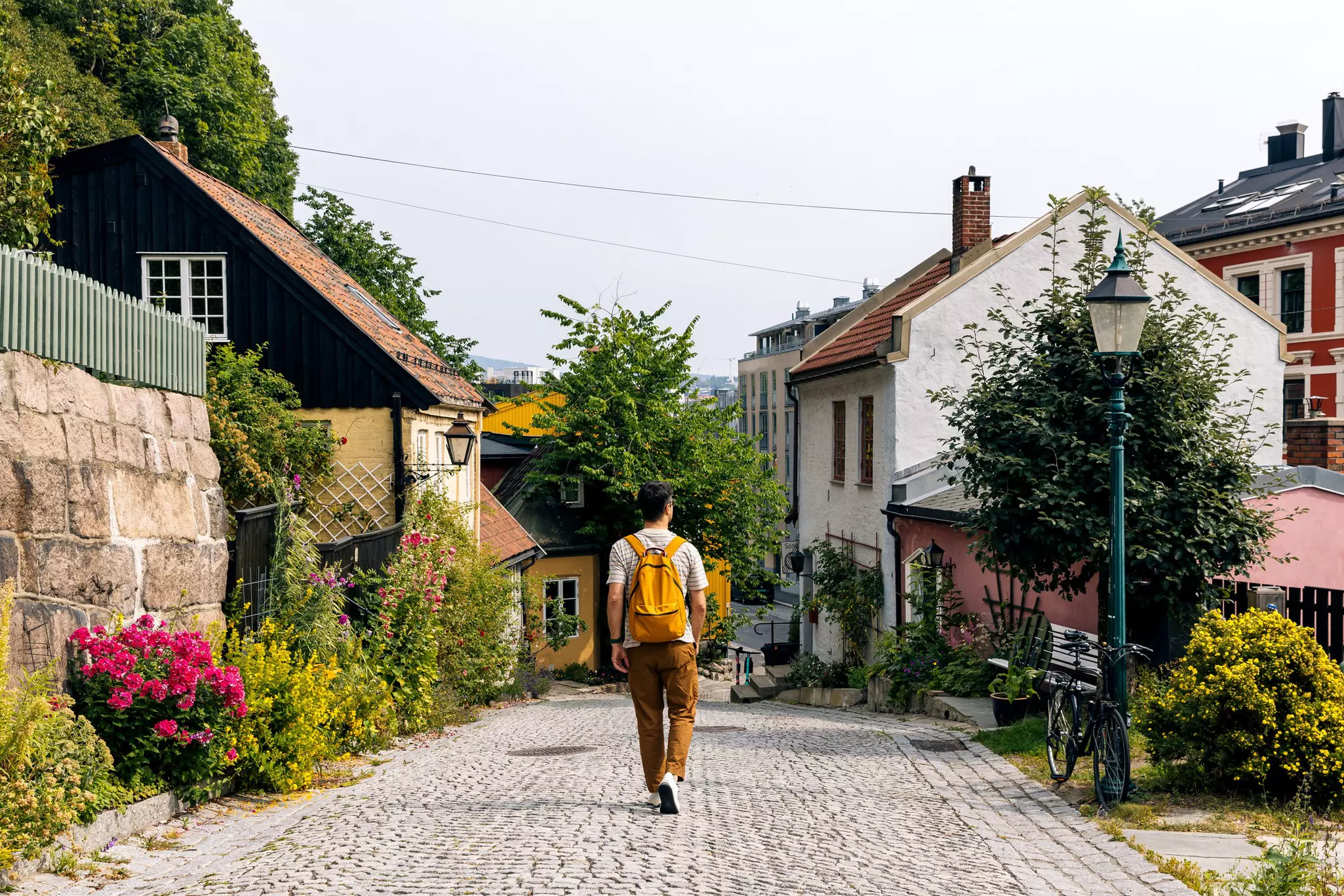 Rear view of a man with backpack walking on a cobblestone street surrounded by historic houses on a gray-ish day.