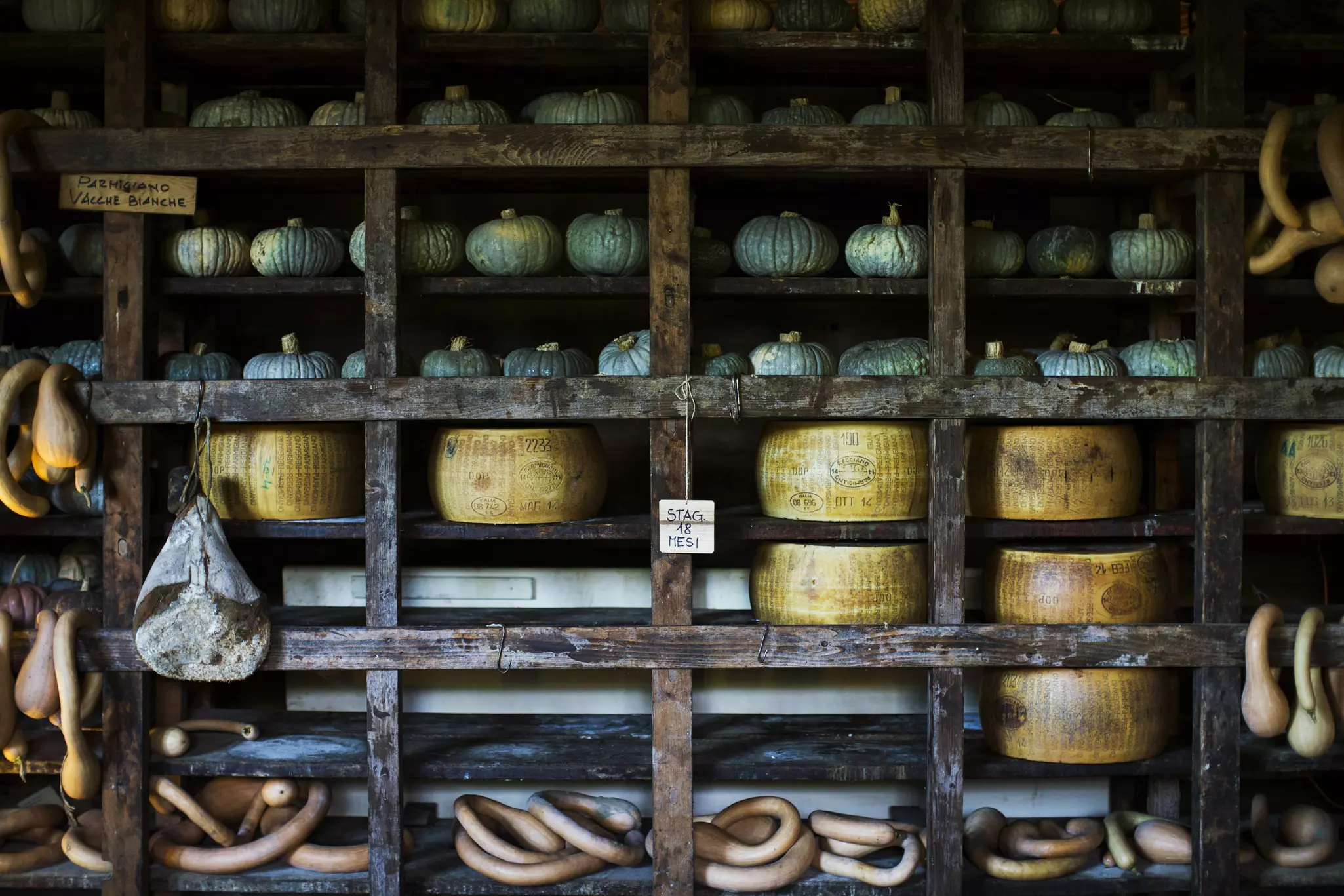 Wooden storage racks of pumpkins and Parmigiano Reggiano cheeses in Emilia-Romagna, Italy.