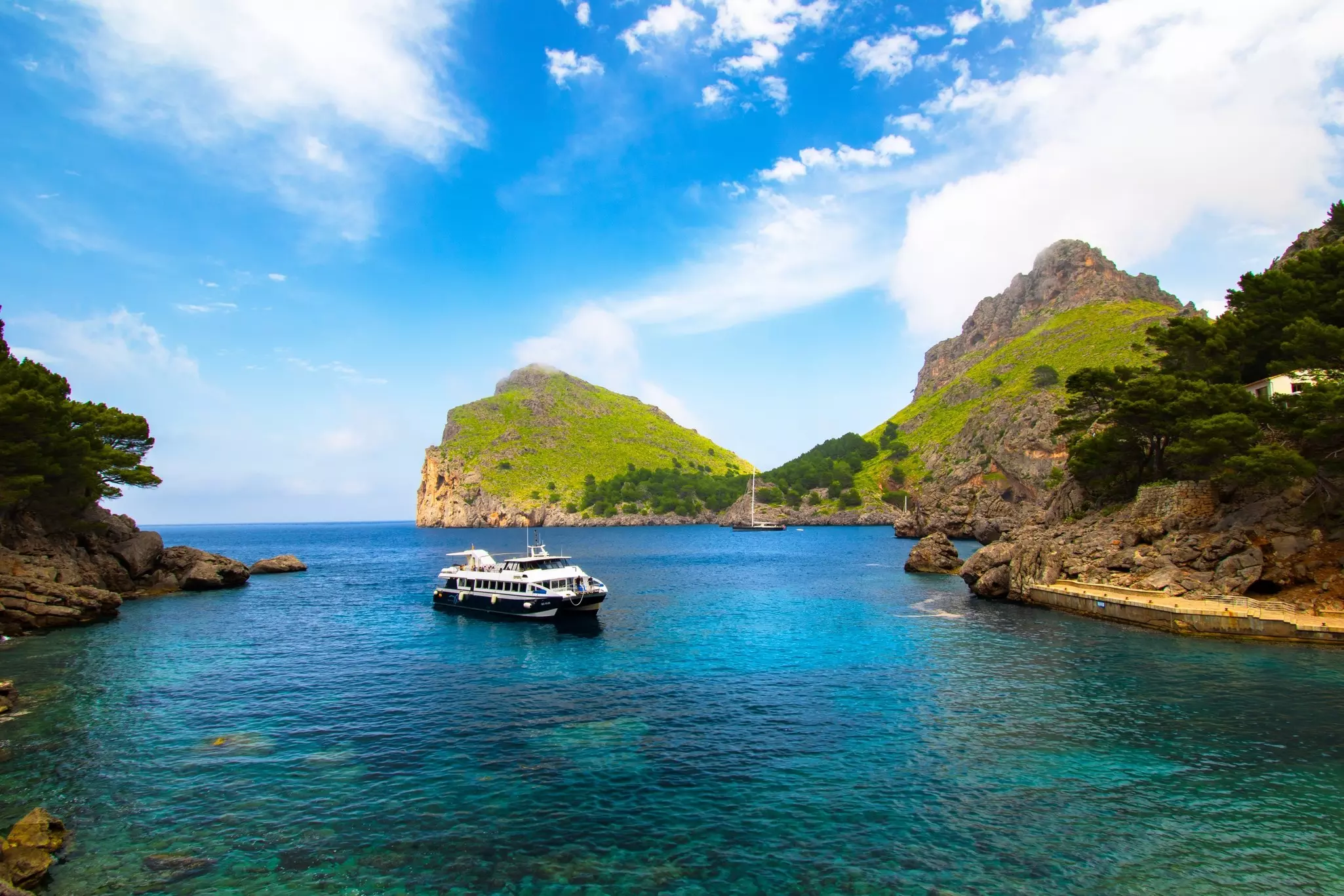 Passenger ferry in a cove surrounded by grassy cliffs and clear blue sea on a sunny day.