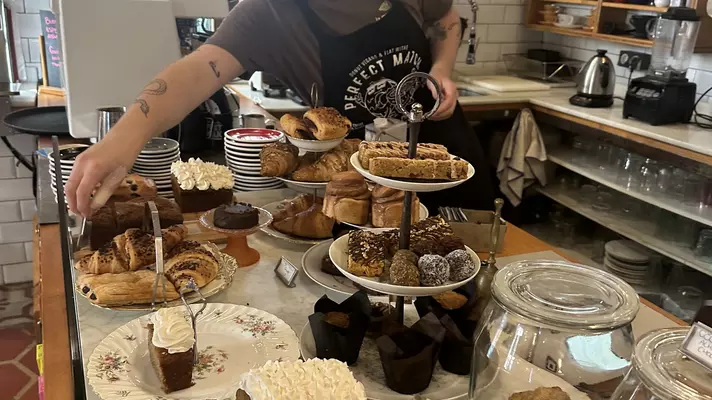 A server wearing a black T-shirt and full blue apron. She is carrying two plates of food on her arm