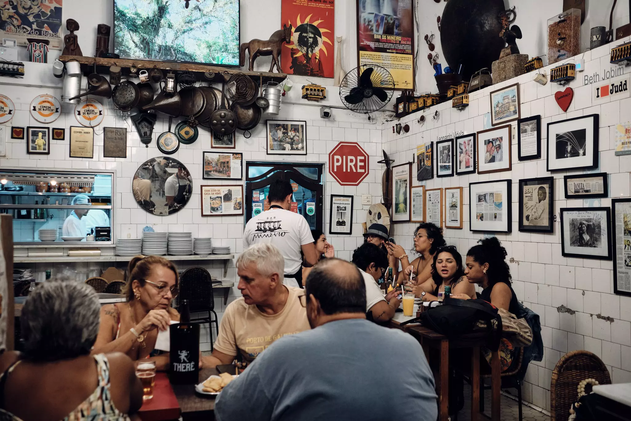 People sit at tables in a room; the walls are covered in framed pictures.