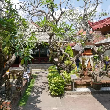 Frangipani trees, stone statues and a paved path in a Balinese courtyard with red-tiled roofs, Sanur, Bali