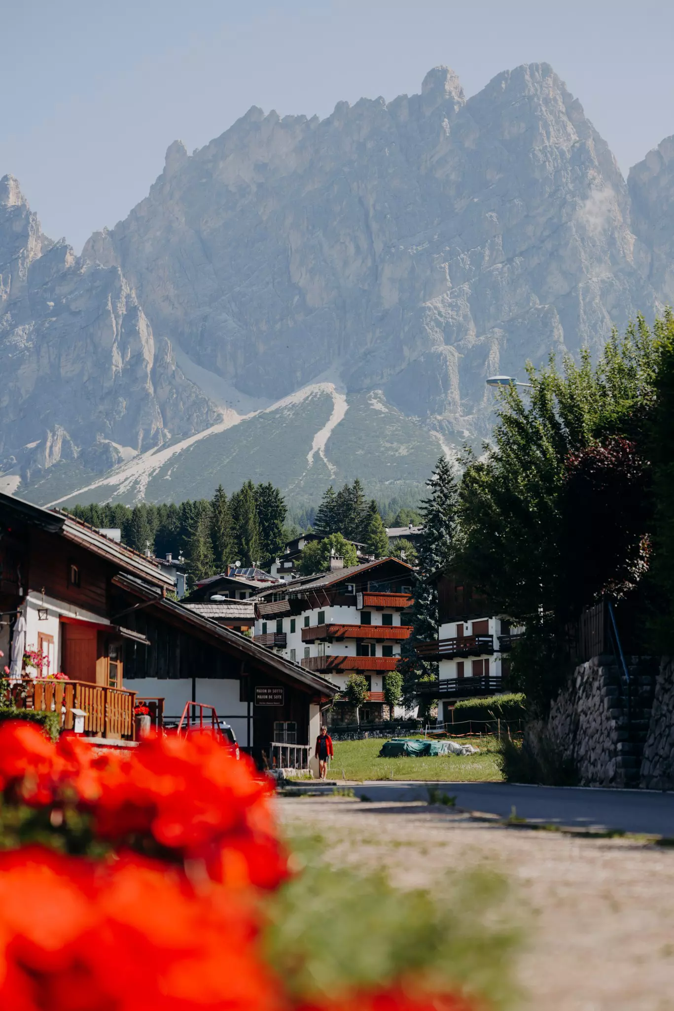 A small town in the shadow of mountains on a summer's day, with bright red flowers filling flower boxes outside chalet-style buildings.