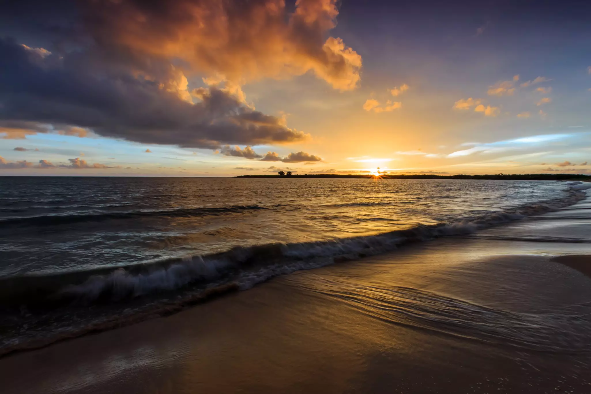 Sunset over waves, with dramatic clouds, at a sandy beach in Cambodia.