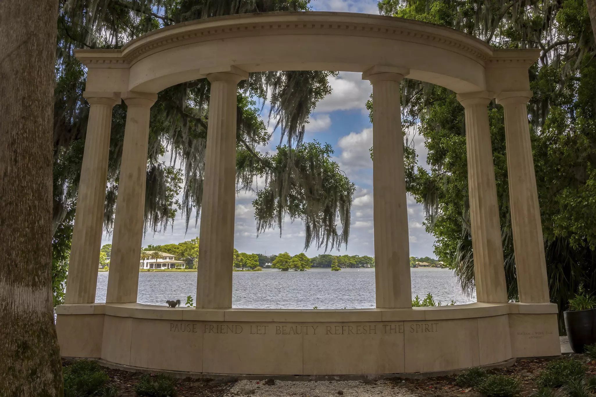 View of a lake through a structure with pillars engraved with the phrase "Pause friend let beauty refresh the spirit"