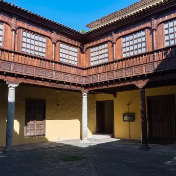 Two-storey courtyard with a carved dark-wood gallery above yellow walls and pale stone columns.