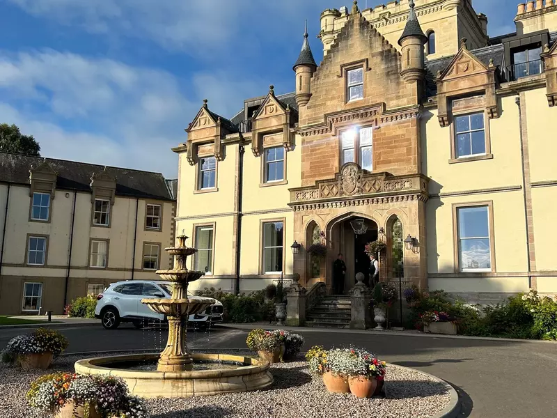 A driveway curves around a fountain in front of a hotel in a historic building.