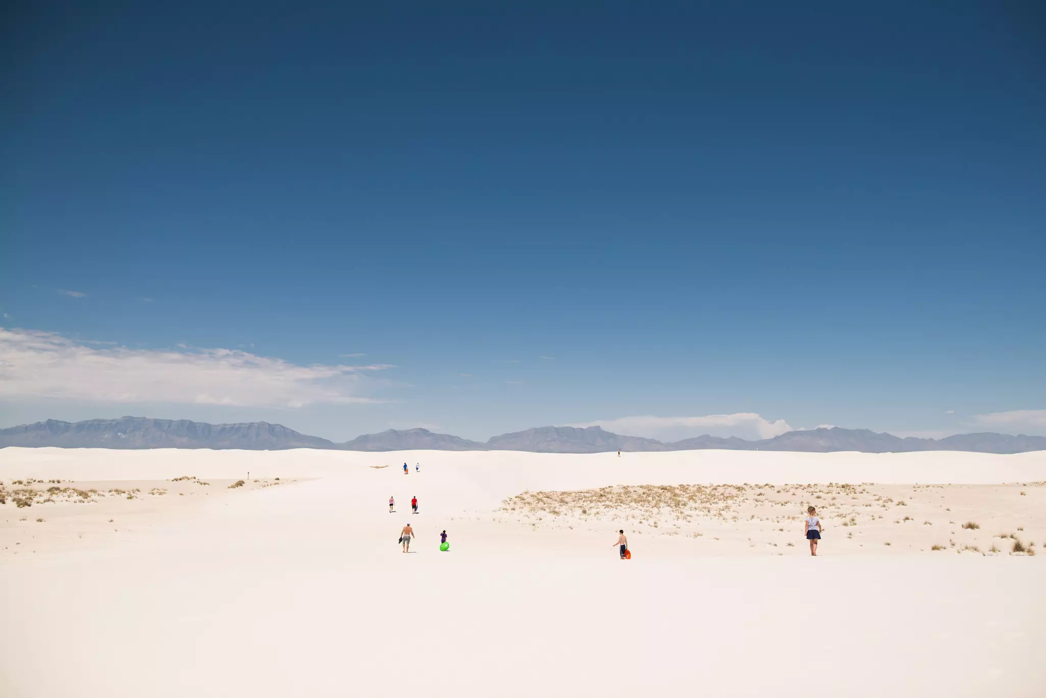 People wander along bright white sand dunes on a sunny day