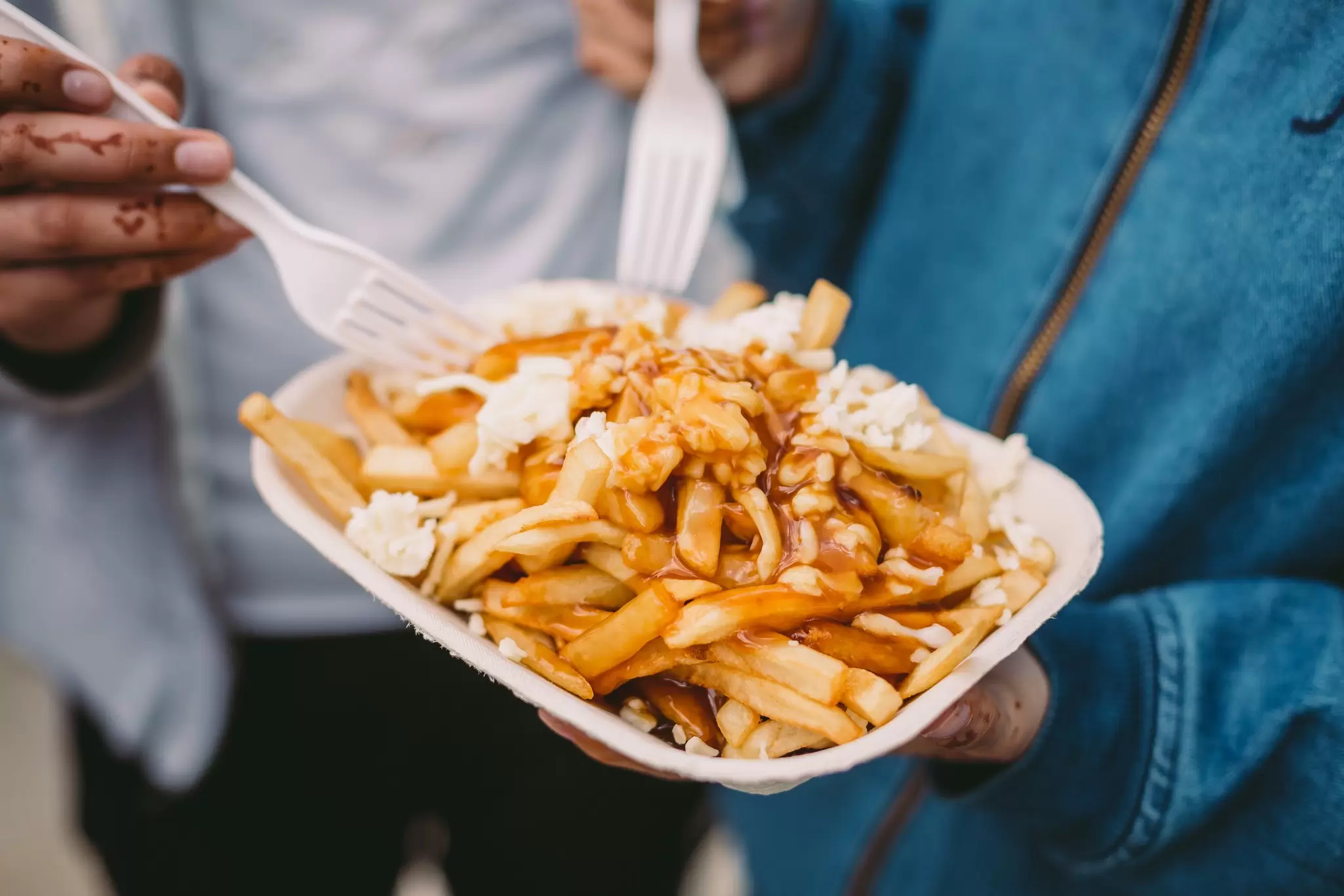 A close-up of people sticking plastic forks into a plate of poutine in Québec, Canada.