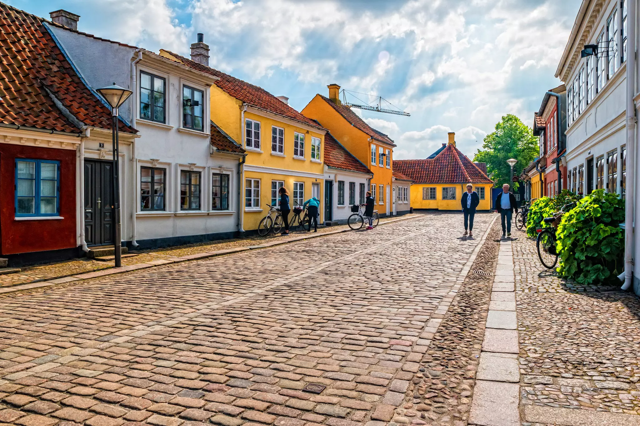People walk on a cobbled street in a city, with historic, brightly painted houses on either side.