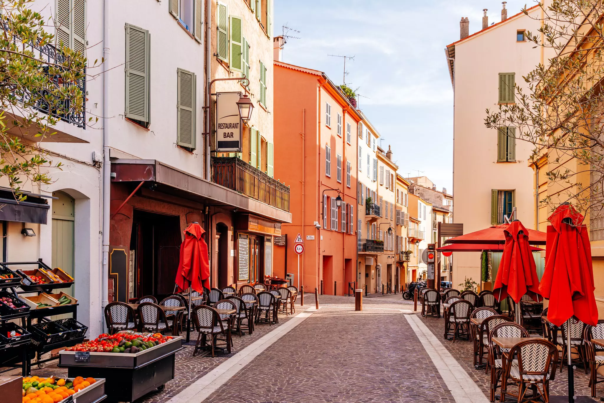 Outdoor tables line a narrow, cobbled street in a historic town in early morning.