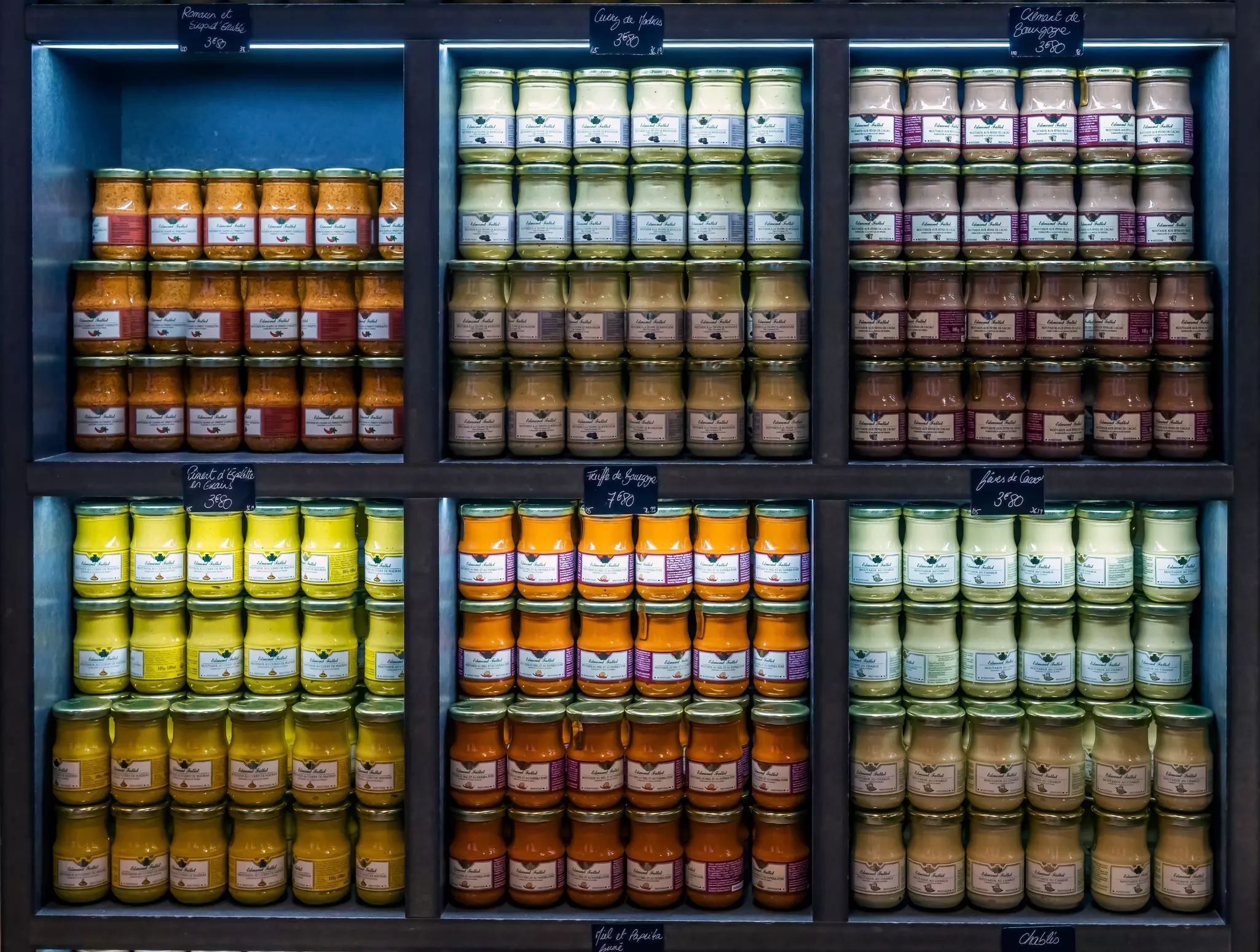 Neat jars of different mustards stacked behind glass in a store.