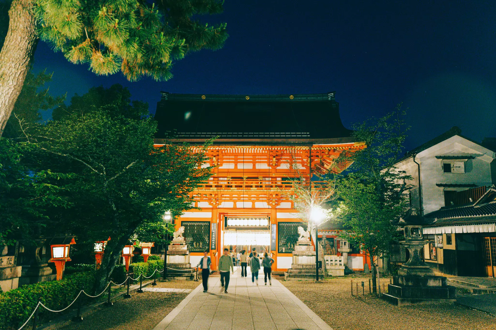 People walk towards a red shrine lit up at night.