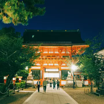 People walk towards a red shrine lit up at night.