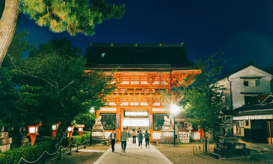 People walk towards a red shrine lit up at night.