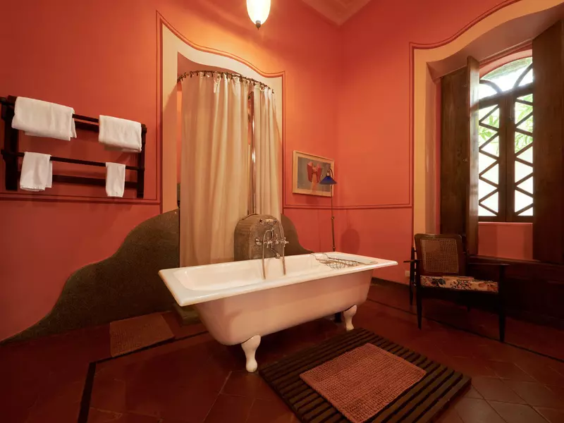 A freestanding bathtub in a hotel bathroom with red walls.