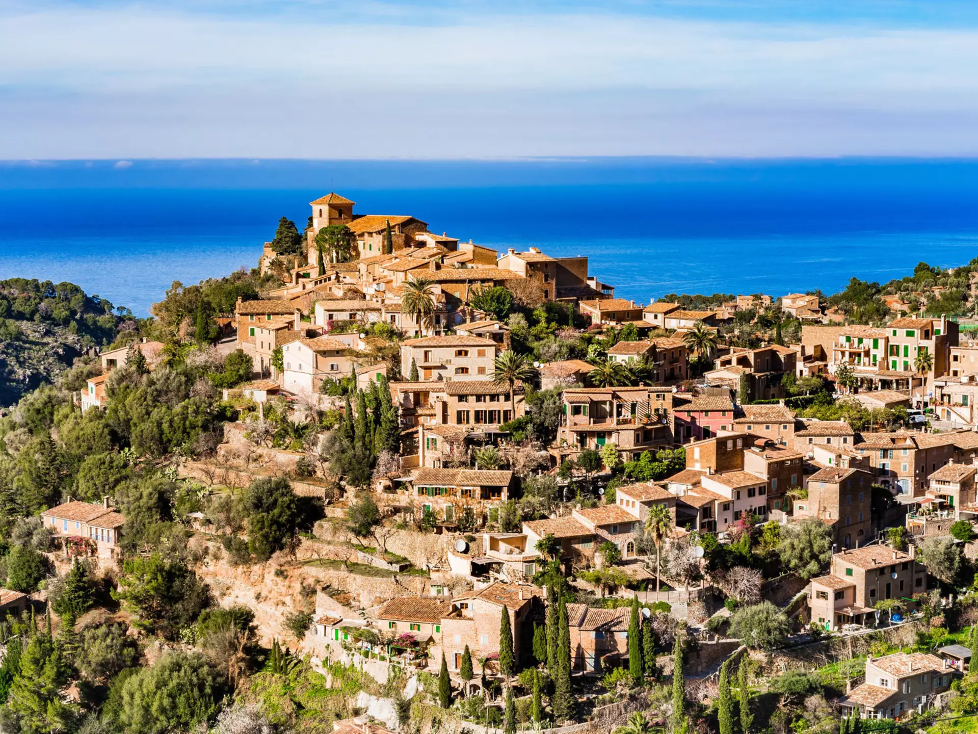 A gorgeous hilltop village bathed in sunshine with the sparkling blue of the ocean in the distance.