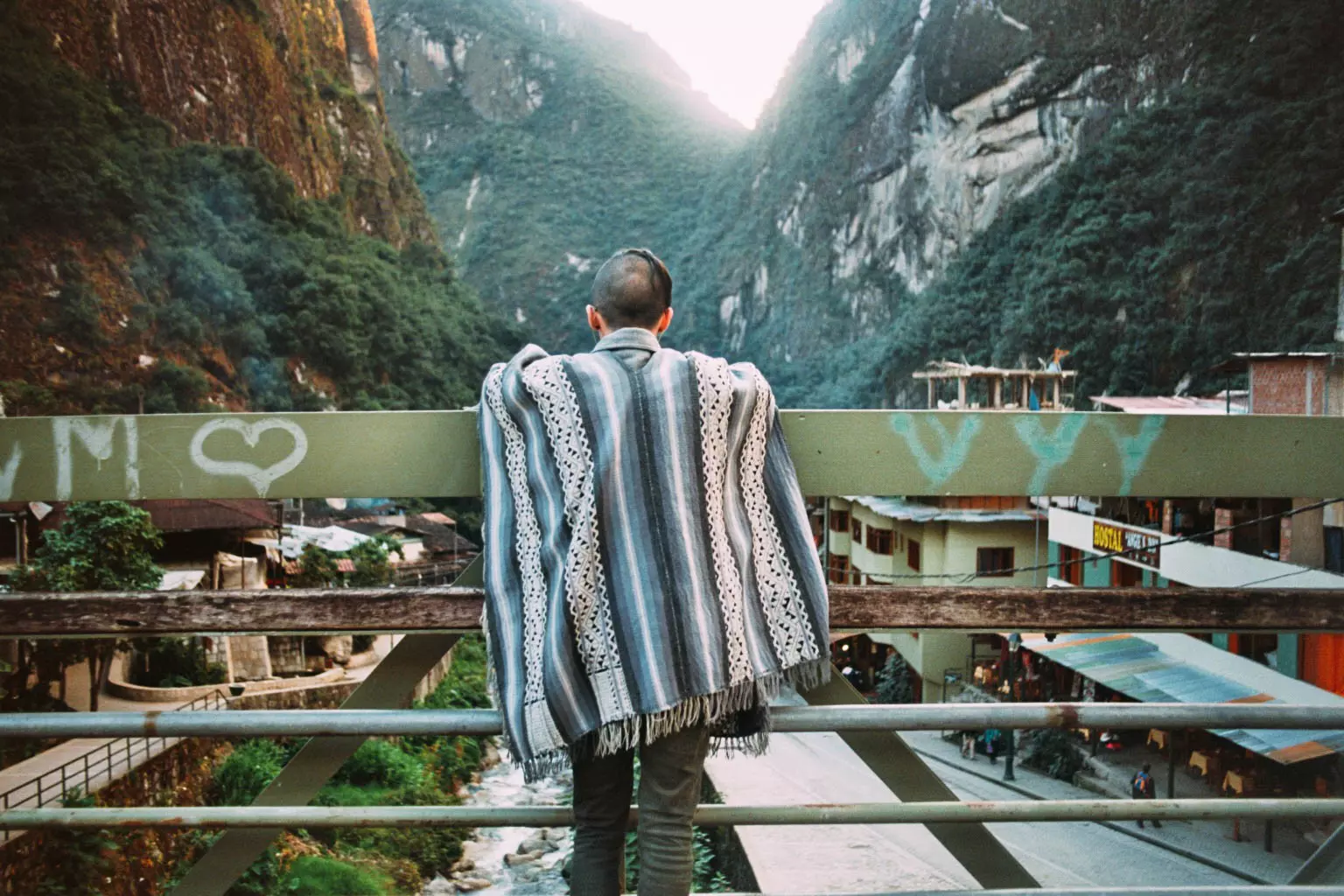 A man wearing a Peruvian poncho leaning on the rails of a bridge at Aguas Calientes.