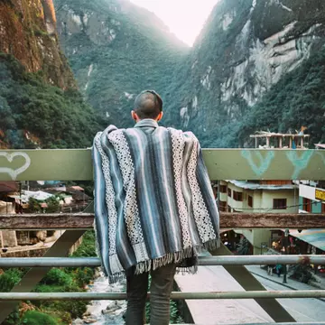 A man wearing a Peruvian poncho leaning on the rails of a bridge at Aguas Calientes.