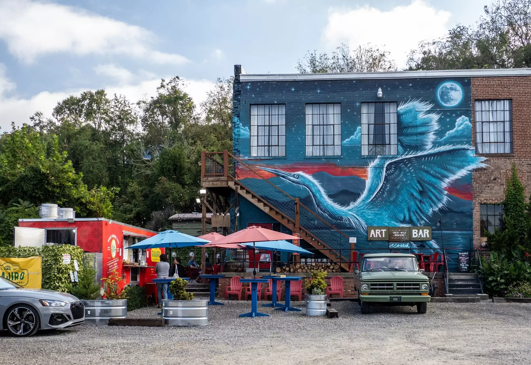 A painted mural of a large bird is seen on the wall of a brick building with tables on the sidewalk outside, Asheville, North Carolina