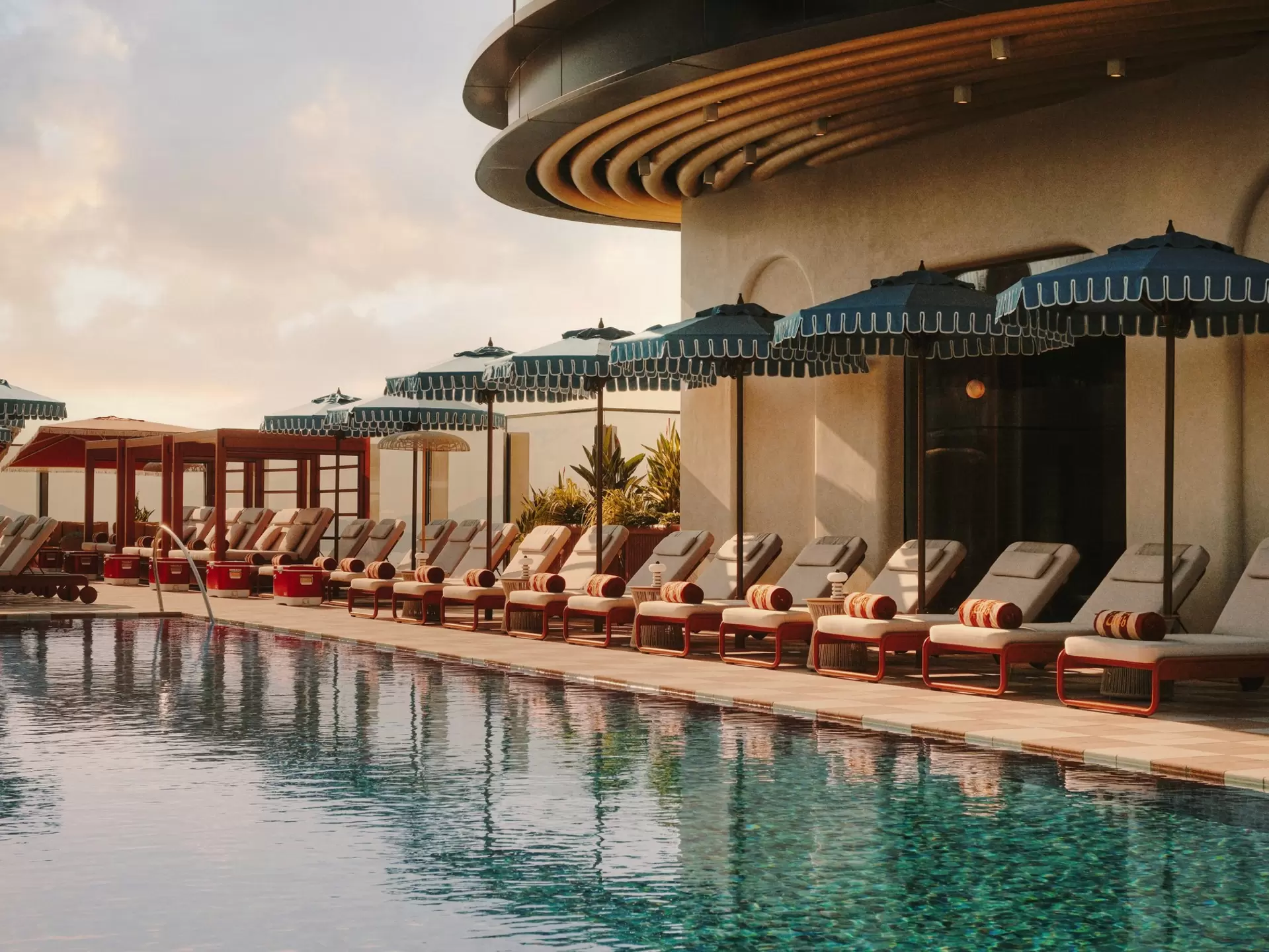 An empty row of loungers with parasols between all of them next to a large pool.