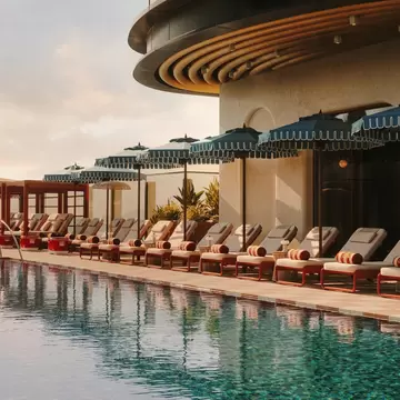 An empty row of loungers with parasols between all of them next to a large pool.