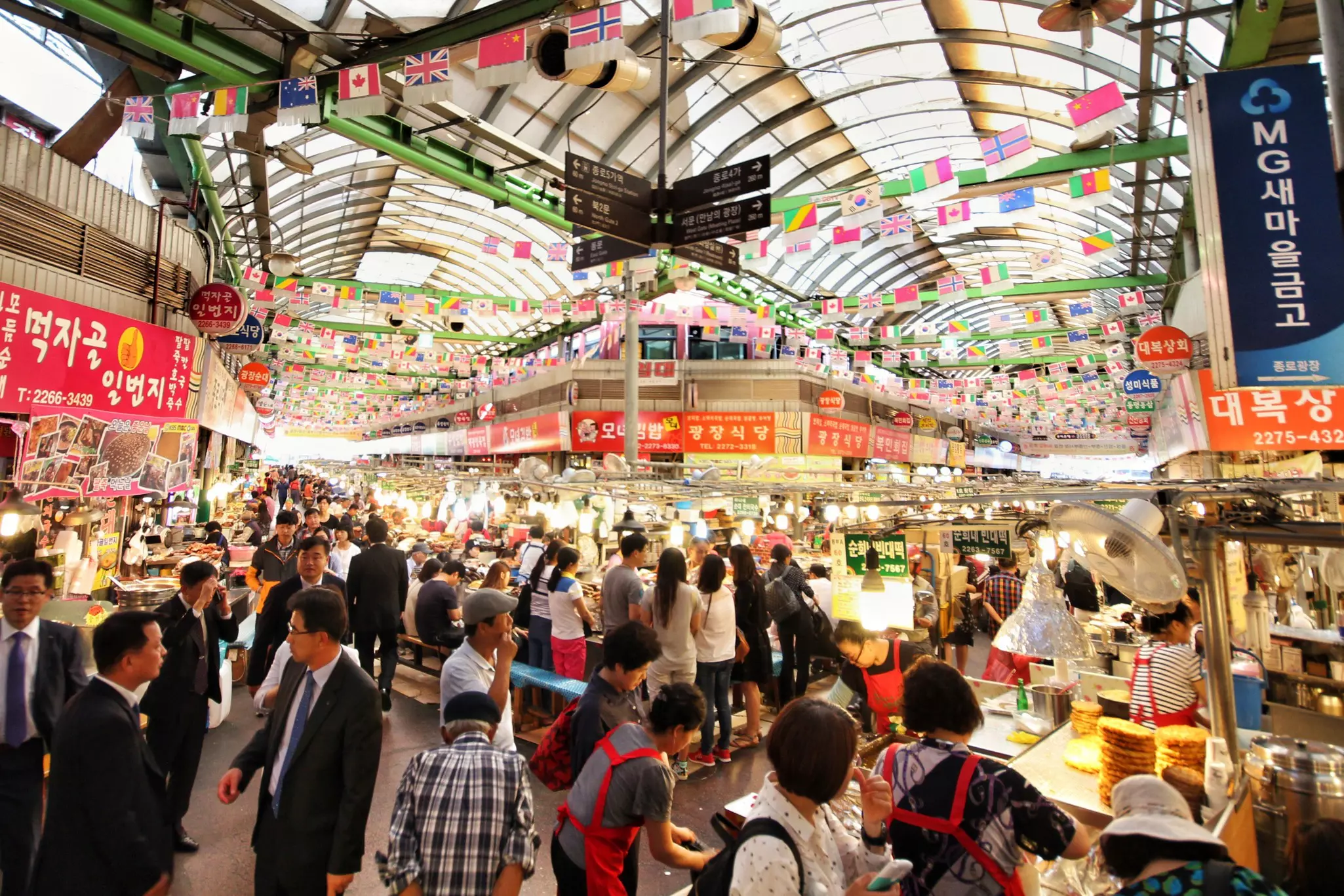 A wide shot of hundreds of people visiting the stalls of a huge, covered food market.