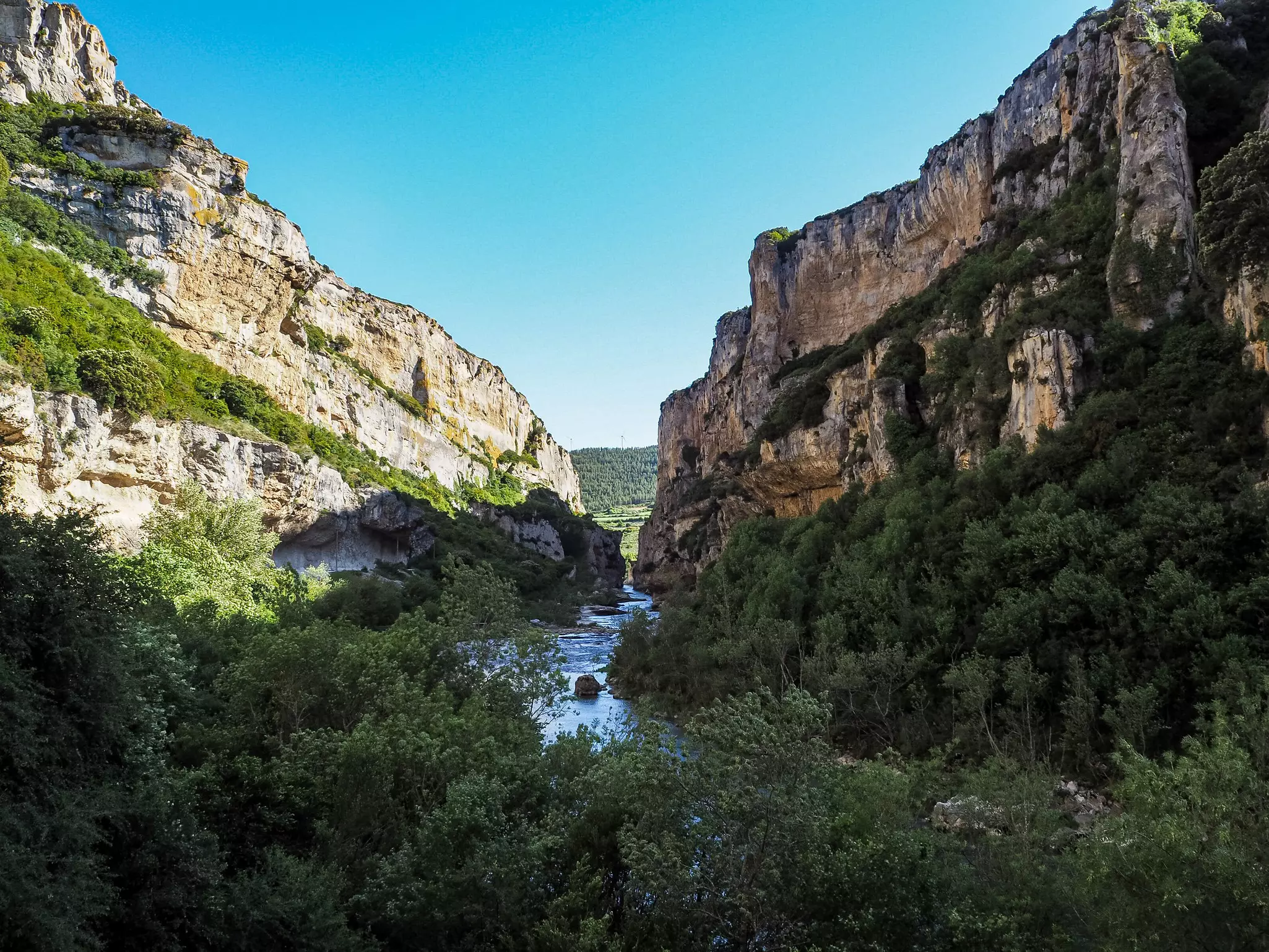 A river flows past walls and grottos in a canyon.