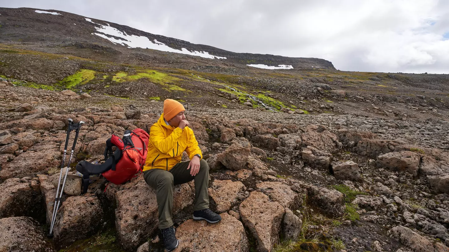 A man sits on a volcanic rock in Iceland, resting during a hike.