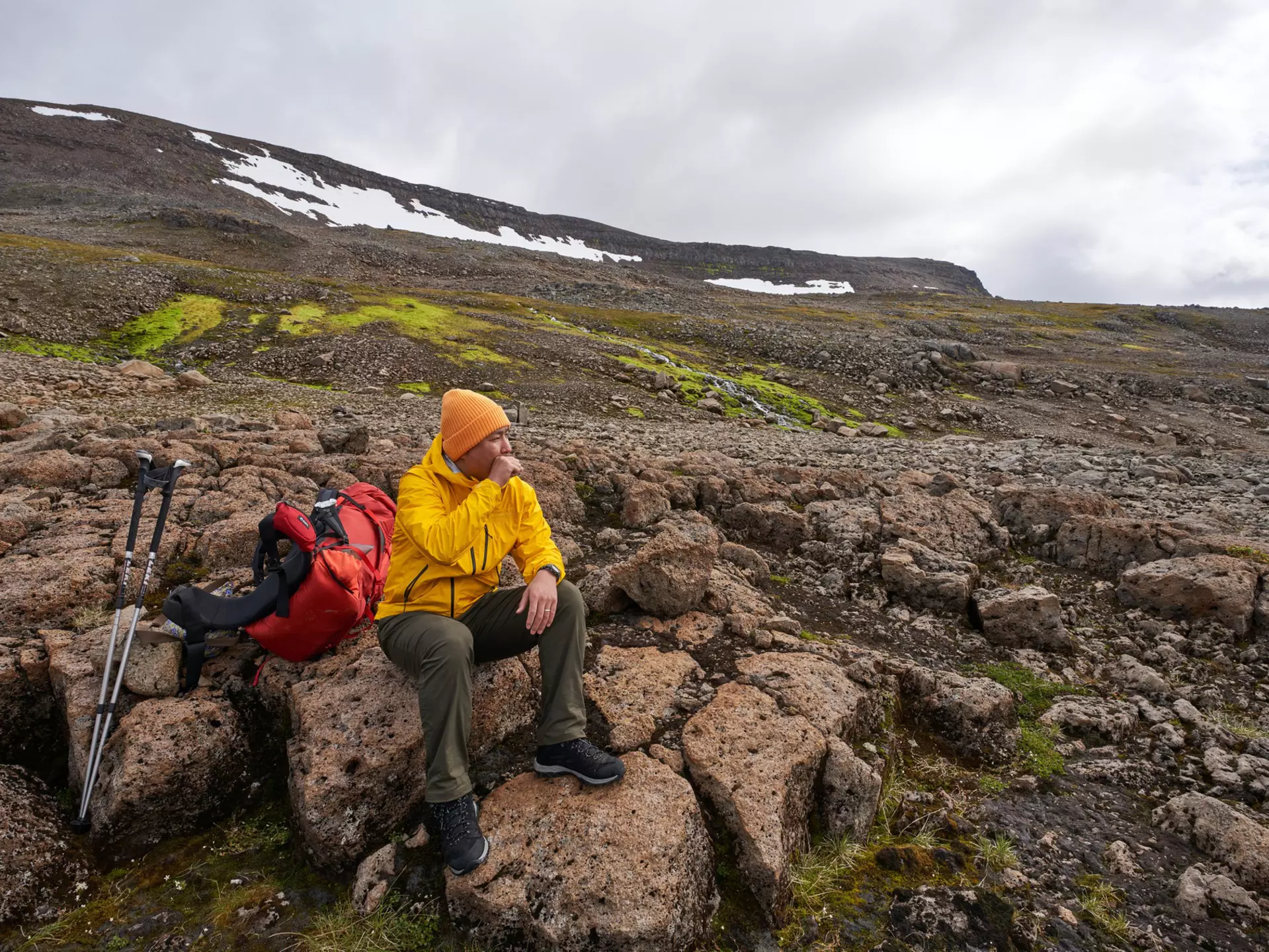 A man sits on a volcanic rock in Iceland, resting during a hike.