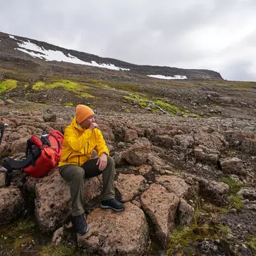 A man sits on a volcanic rock in Iceland, resting during a hike.