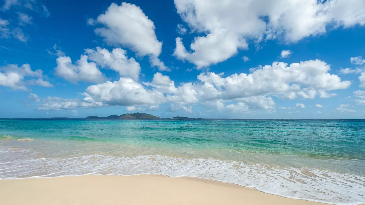 Jost Van Dyke viewed across turquoise Caribbean waters from the white sands of Apple Bay Beach on Tortola, BVI