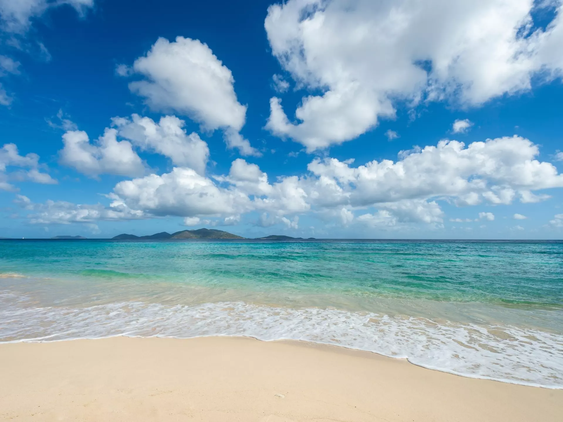 Jost Van Dyke viewed across turquoise Caribbean waters from the white sands of Apple Bay Beach on Tortola, BVI