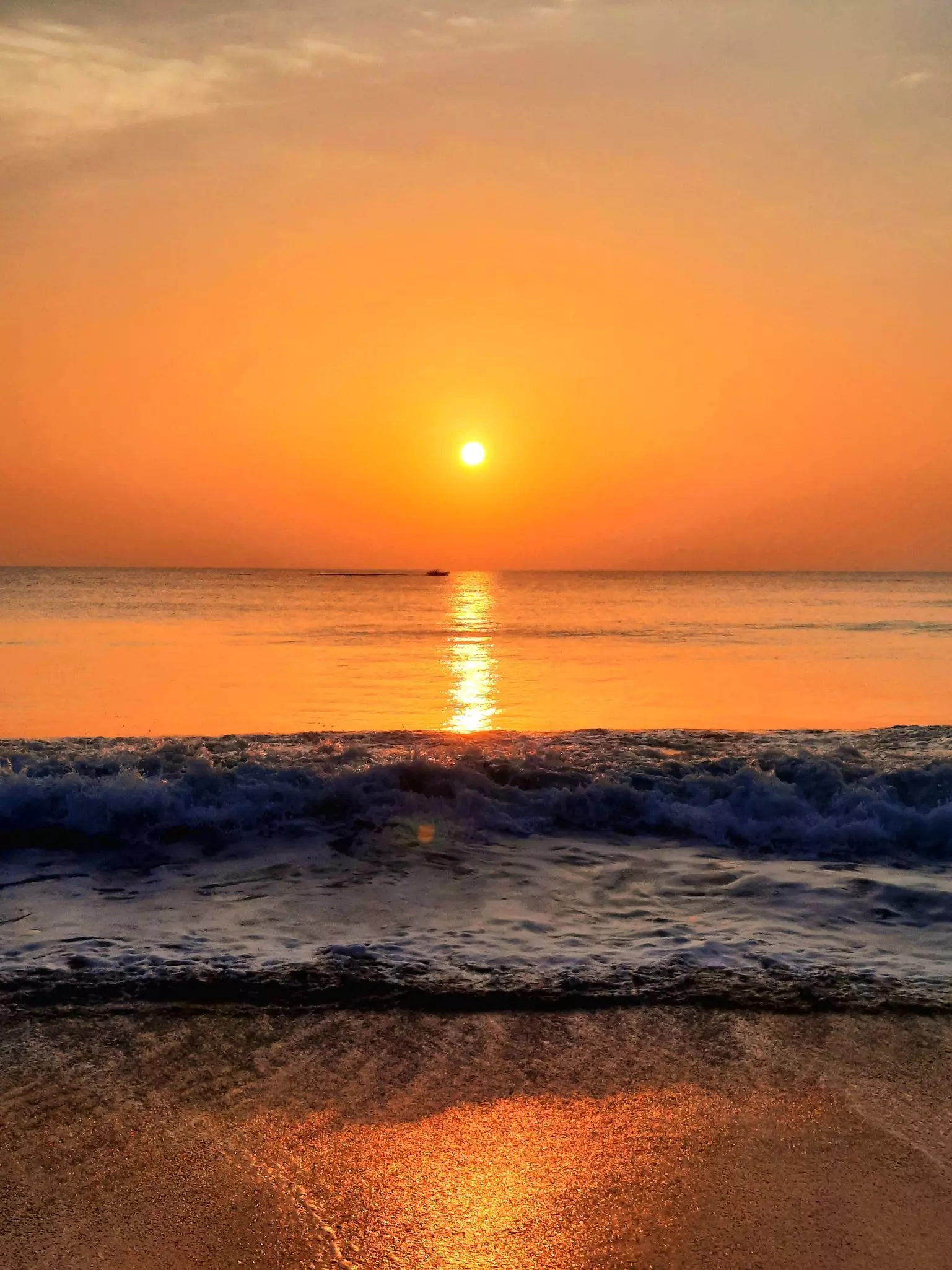 Waves crashing on a beach under a bright orange sky at sunrise