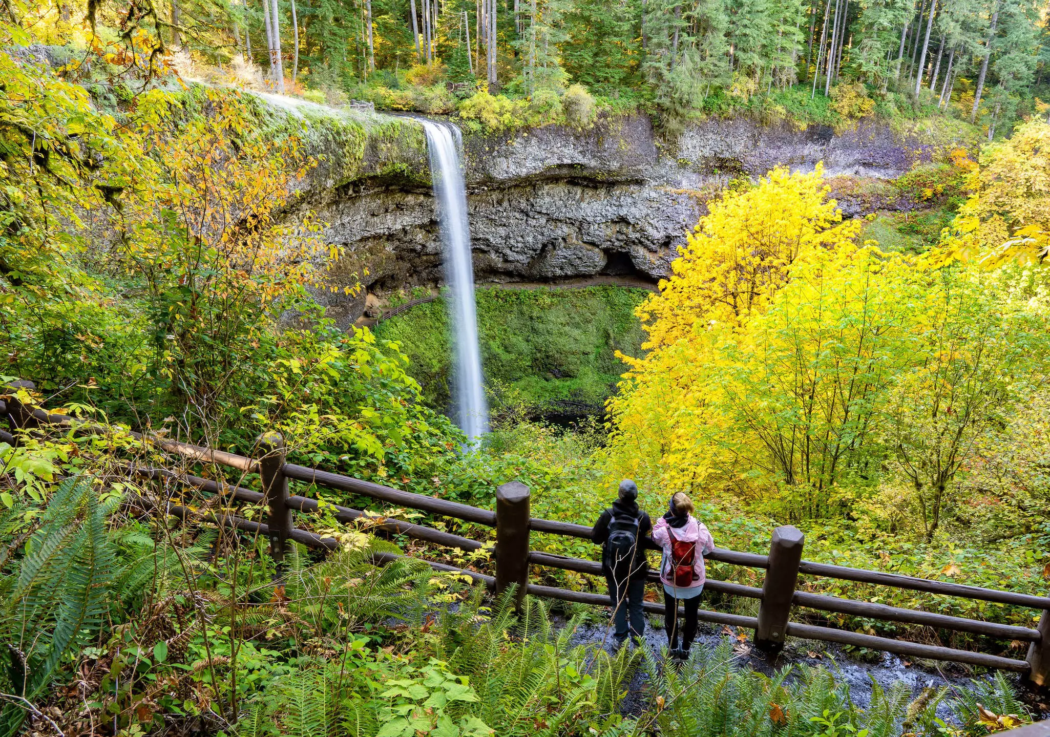 Two women looking at South falls and trees in autumn season showing fall colors, in Silver Falls State Park near Silverton, Oregon