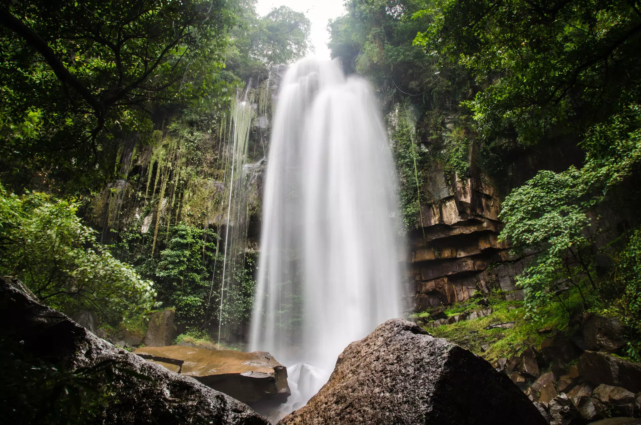 A waterfall over rocks amid dense green vegetation at a national park in Cambodia.