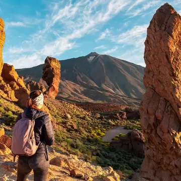 Woman with backpack hiking with scenic golden hour sunrise morning view on unique rock formation Roque Cinchado, Roques de Garcia, Tenerife, Canary Island, Spain, Europe. Pico del Teide volcano summit