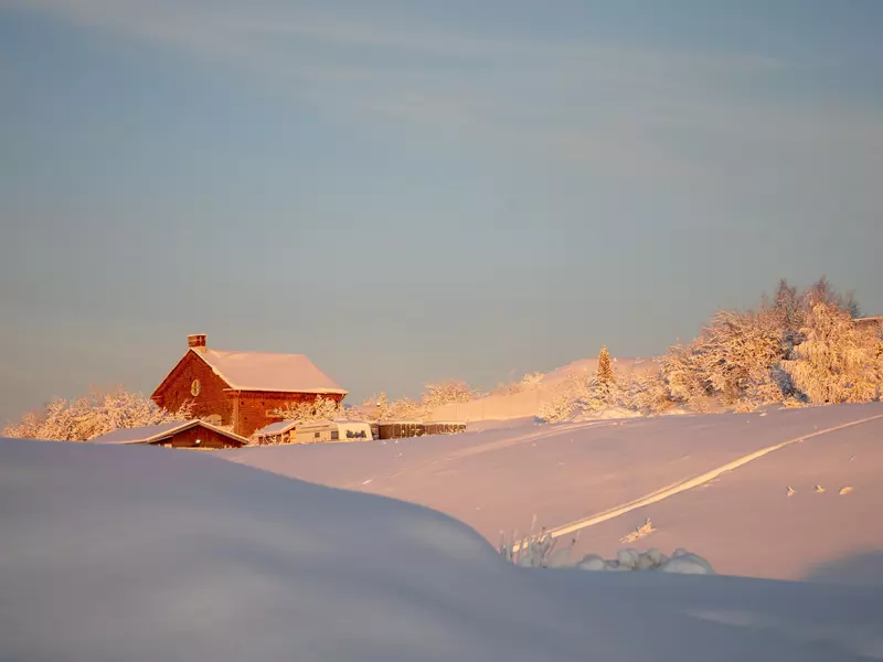 Red building with snow on roof amidst a snowy scene under a cold blue sky