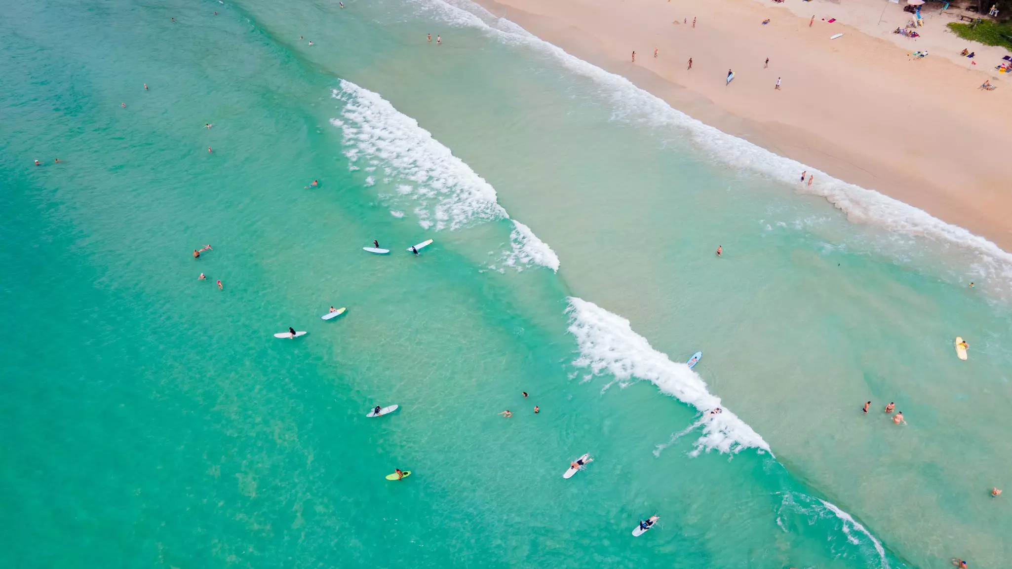 View of surfers riding waves from above as waves lap the shore