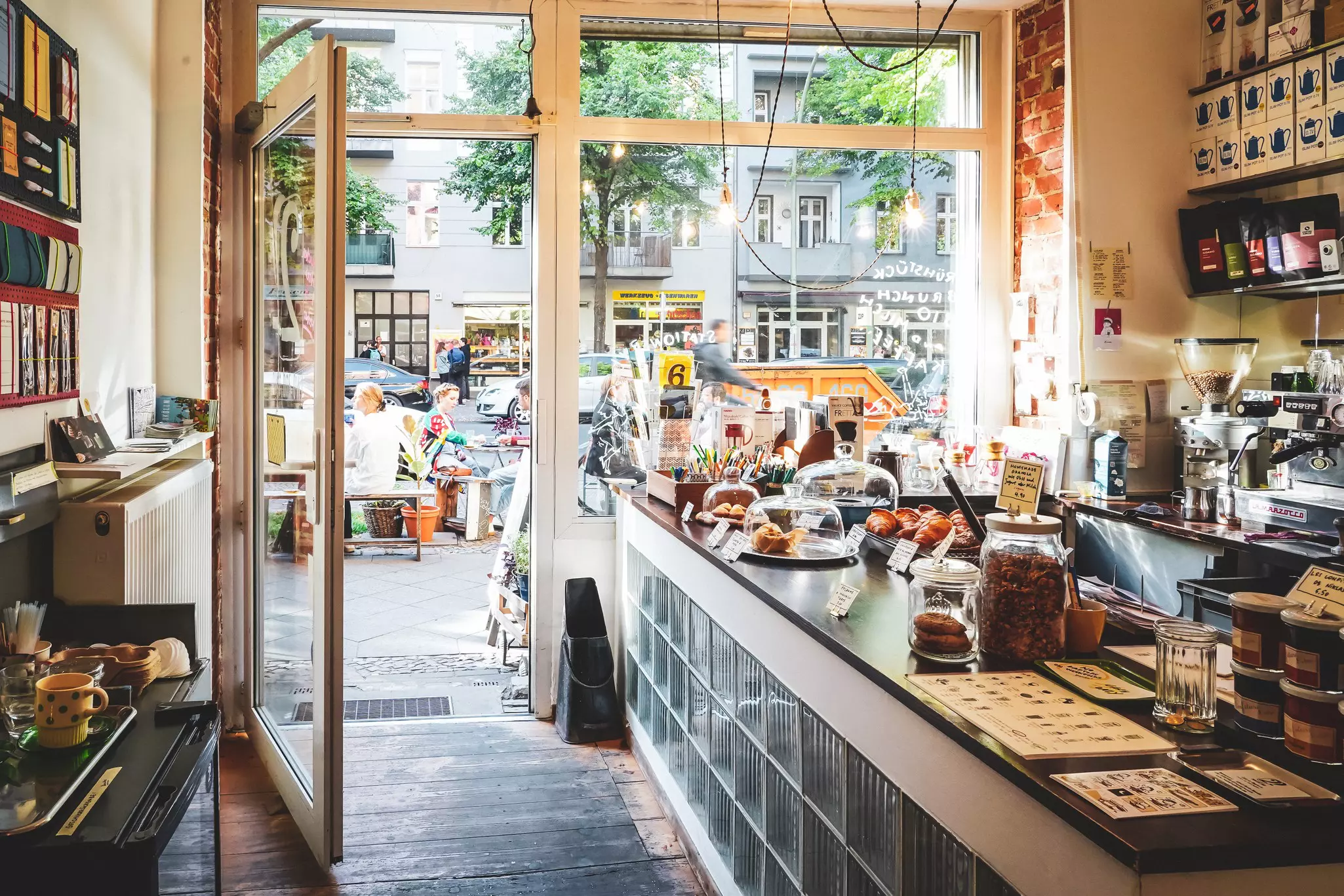 A cafe with an outdoor patio has its doors open to a busy street in a city