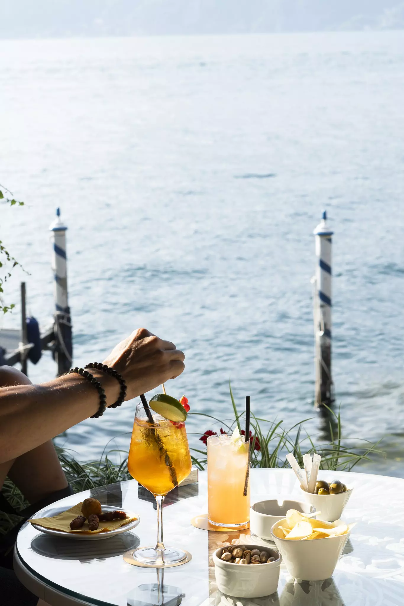 A few drinks and a collection of snacks on a table in front of the lake.