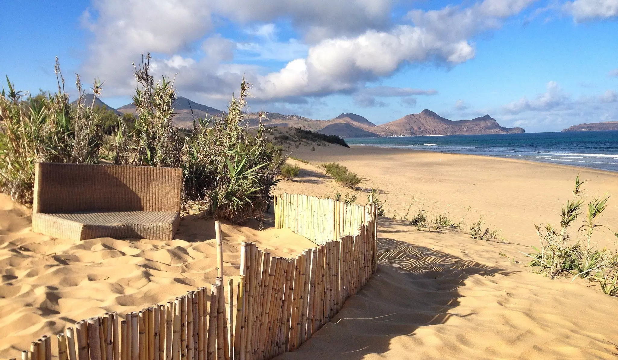 A golden sandy beach, with dry mountains in the distance.