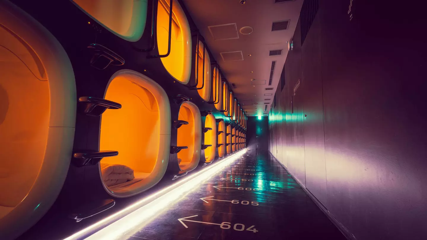 A corridor with one-person sleeping pods to one side and numbered arrows on the floor indicating which pod is which