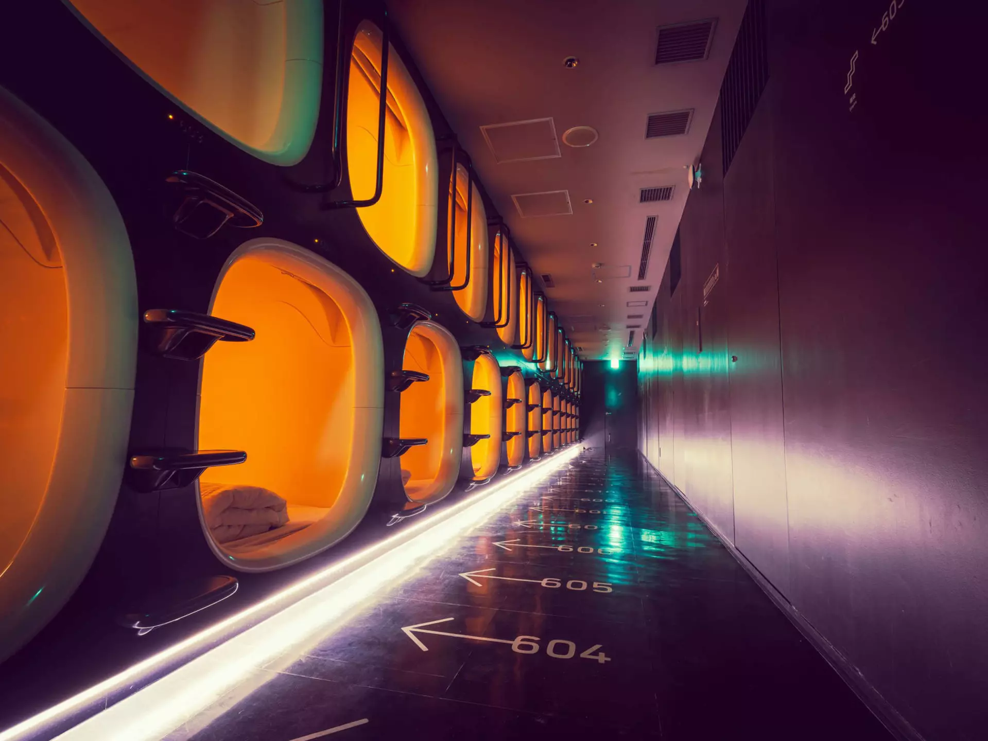 A corridor with one-person sleeping pods to one side and numbered arrows on the floor indicating which pod is which