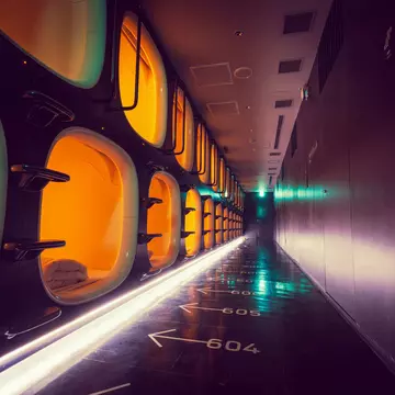 A corridor with one-person sleeping pods to one side and numbered arrows on the floor indicating which pod is which