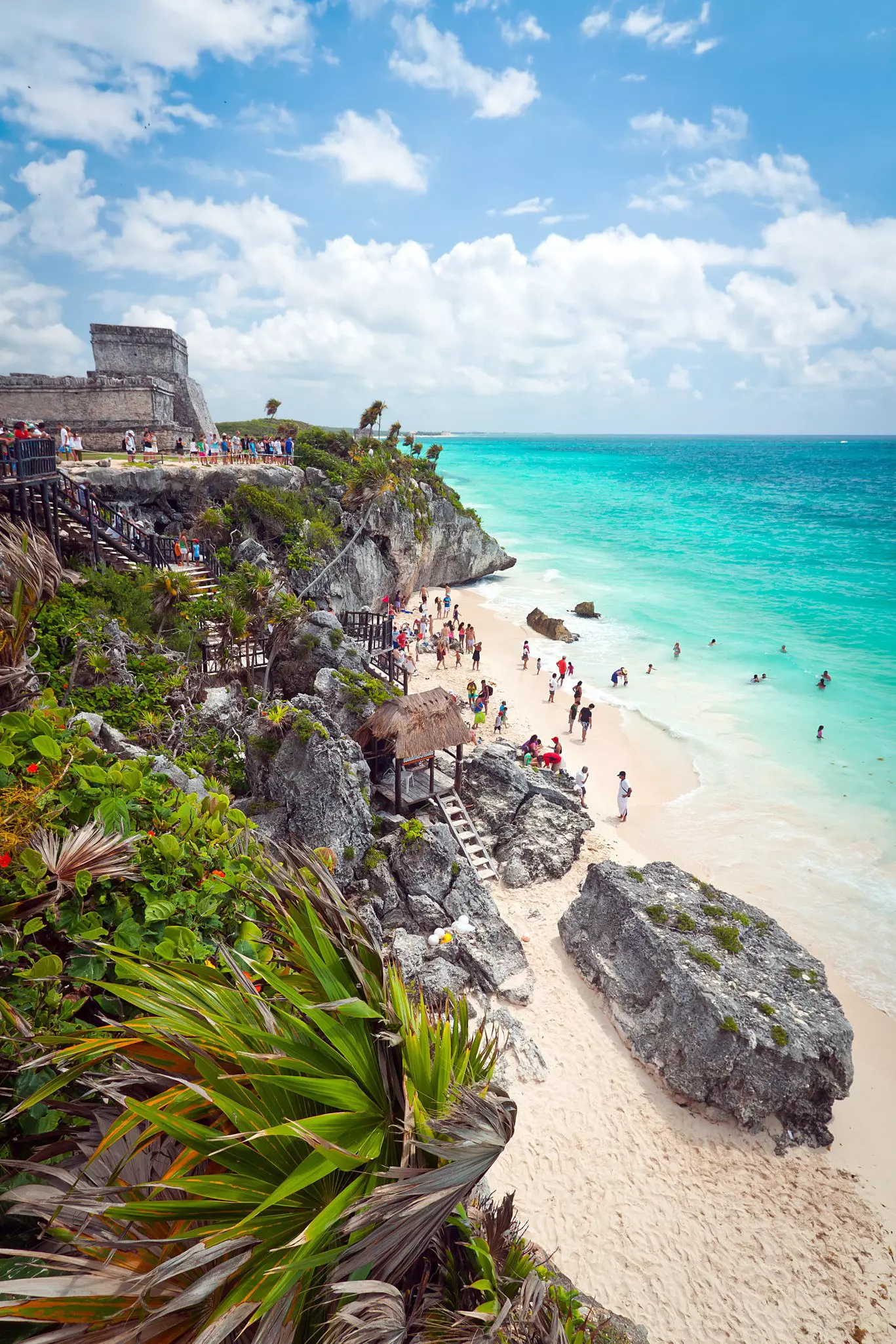 Ancient stone ruins stand in a block on a clifftop above a pristine white sand beach