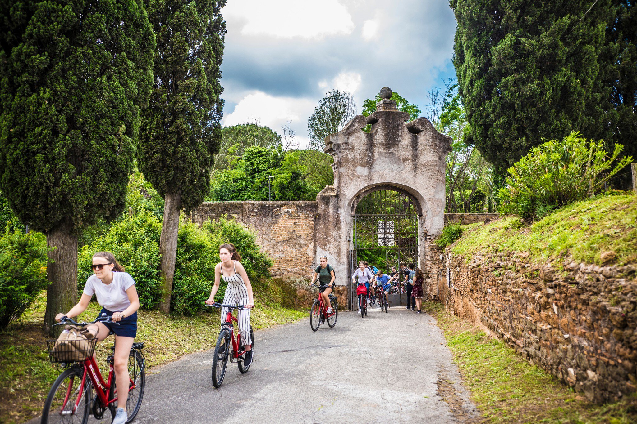 ROME, ITALY - May 2018: Cycling people at the entrance gate to the Catacombe di San Callisto cave historical town in Rome, Italy; Shutterstock ID 1301255716; purchase_order: 65050; job: poi; client: ; other: