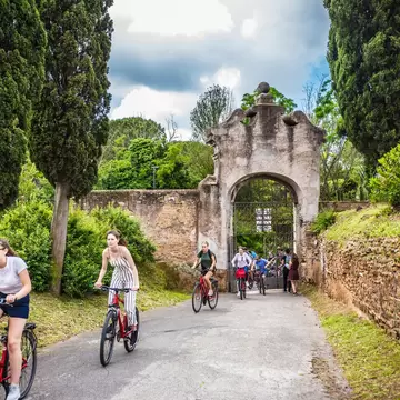 ROME, ITALY - May 2018: Cycling people at the entrance gate to the Catacombe di San Callisto cave historical town in Rome, Italy; Shutterstock ID 1301255716; purchase_order: 65050; job: poi; client: ; other:
